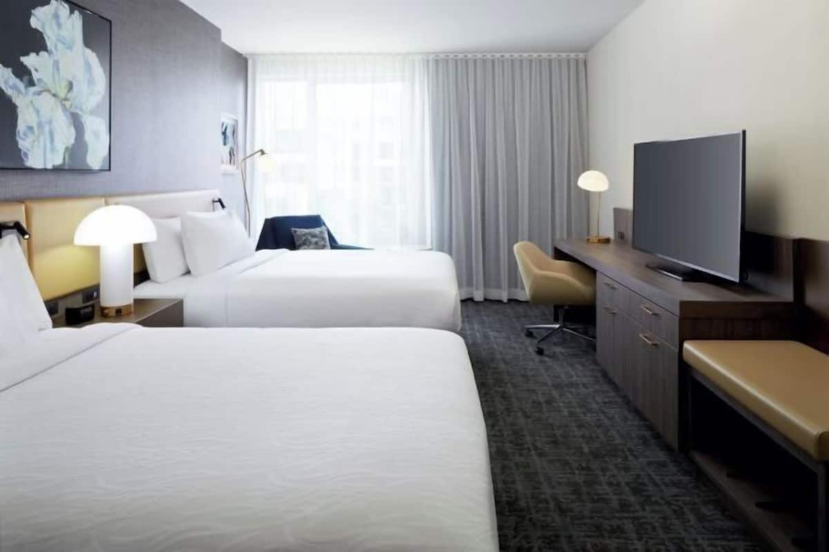 A hotel room with two beds, a TV, a desk, and a chair.