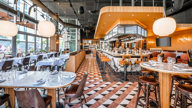 A modern restaurant with a checkered floor, multiple dining tables, and a bar area. - Hilton Garden Inn Montreal Midtown (Montreal)