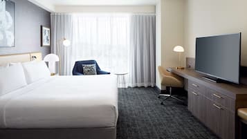 Habitación de hotel con una cama grande, un escritorio con televisor, una silla y una mesita.