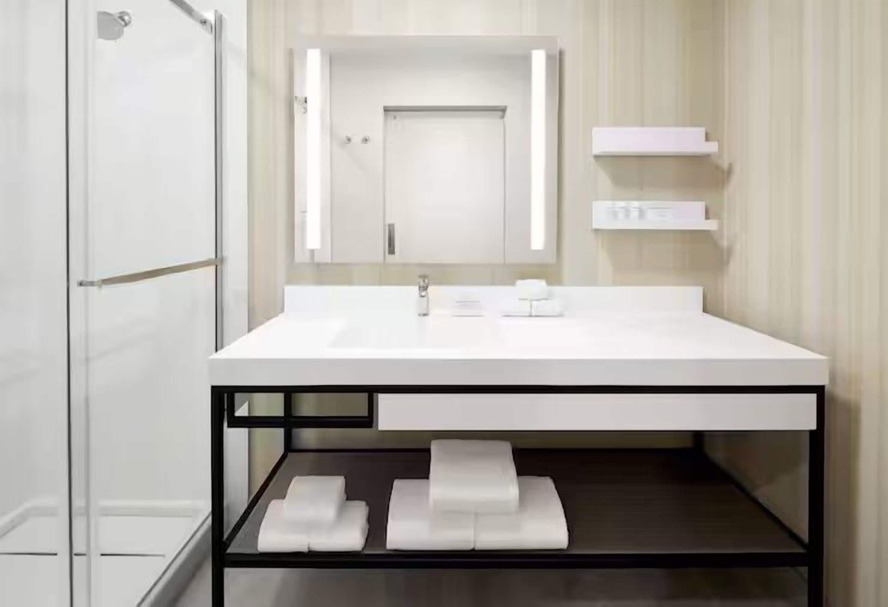 Un baño moderno con un lavamanos blanco, un espejo y una cabina de ducha con paredes de vidrio.