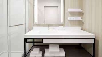 Un baño moderno con un lavamanos blanco, un espejo y una cabina de ducha con paredes de vidrio.