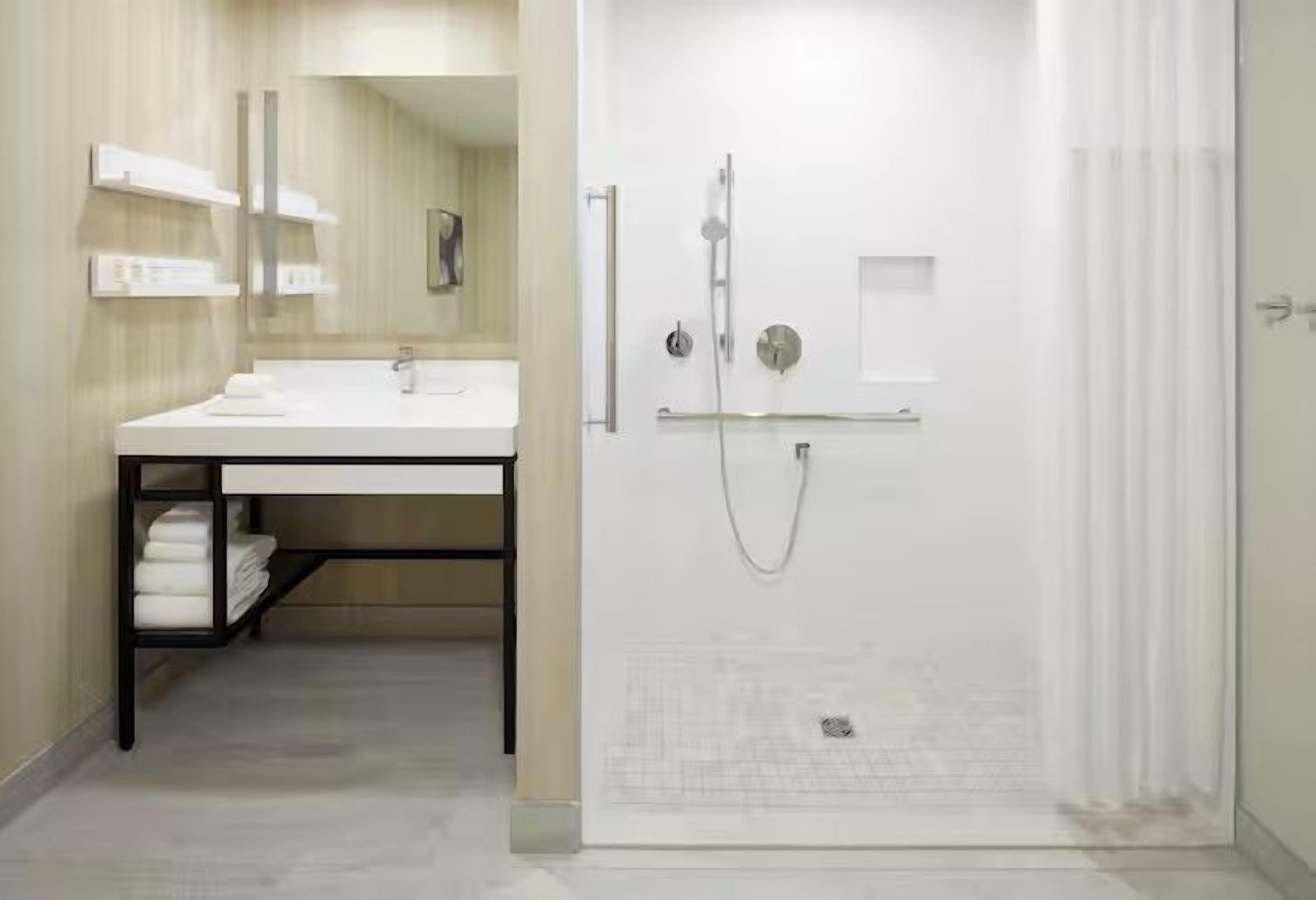 Un baño moderno con ducha, lavabo con espejo y un perchero para toallas.