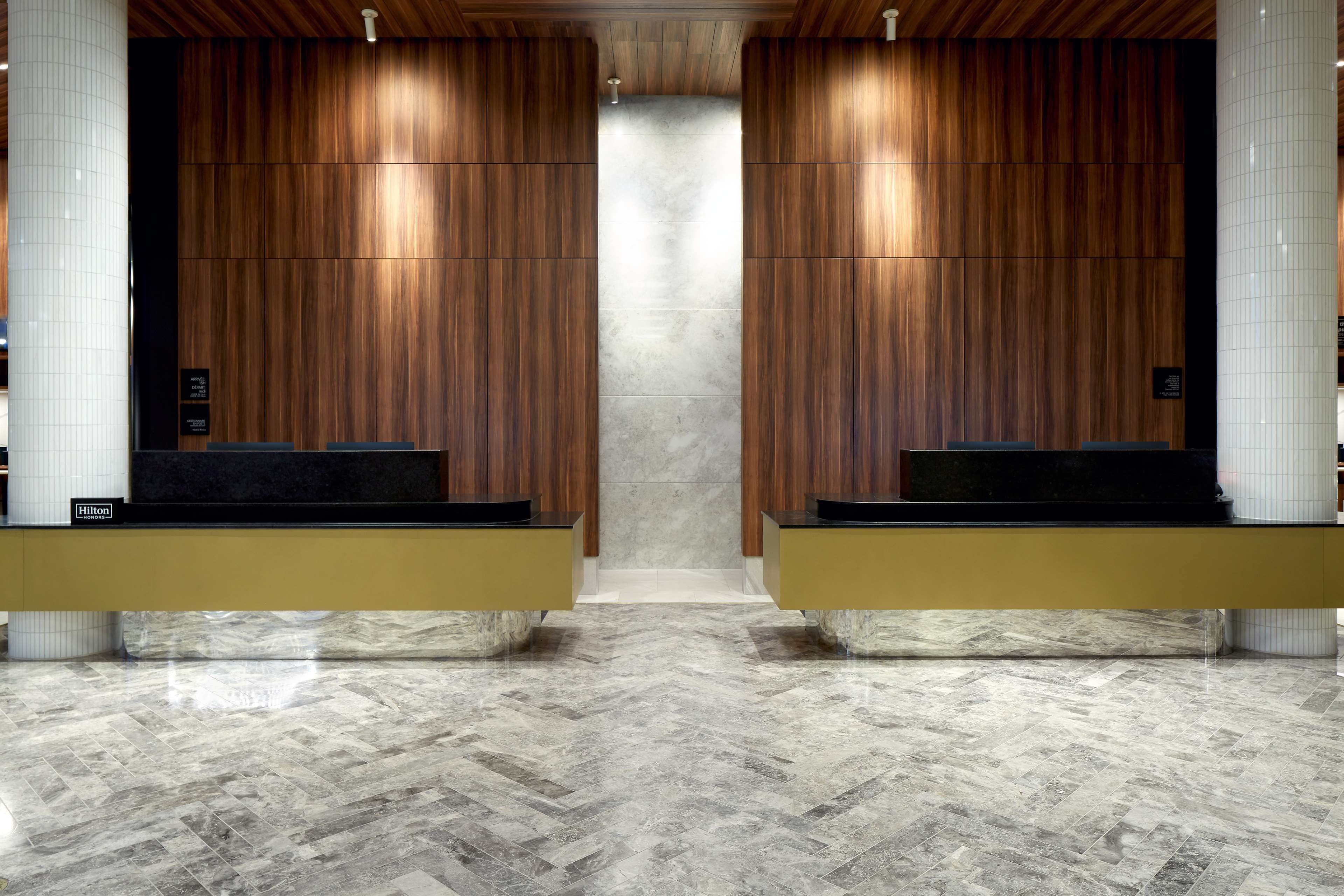 A hotel reception area with wooden panel walls, marble flooring, and two reception desks.