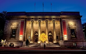 The exterior of The Montreal Museum of Fine Arts at night, featuring classical architecture with columns and a large illuminated sculpture in front. - Hilton Garden Inn Montreal Midtown (Montreal)