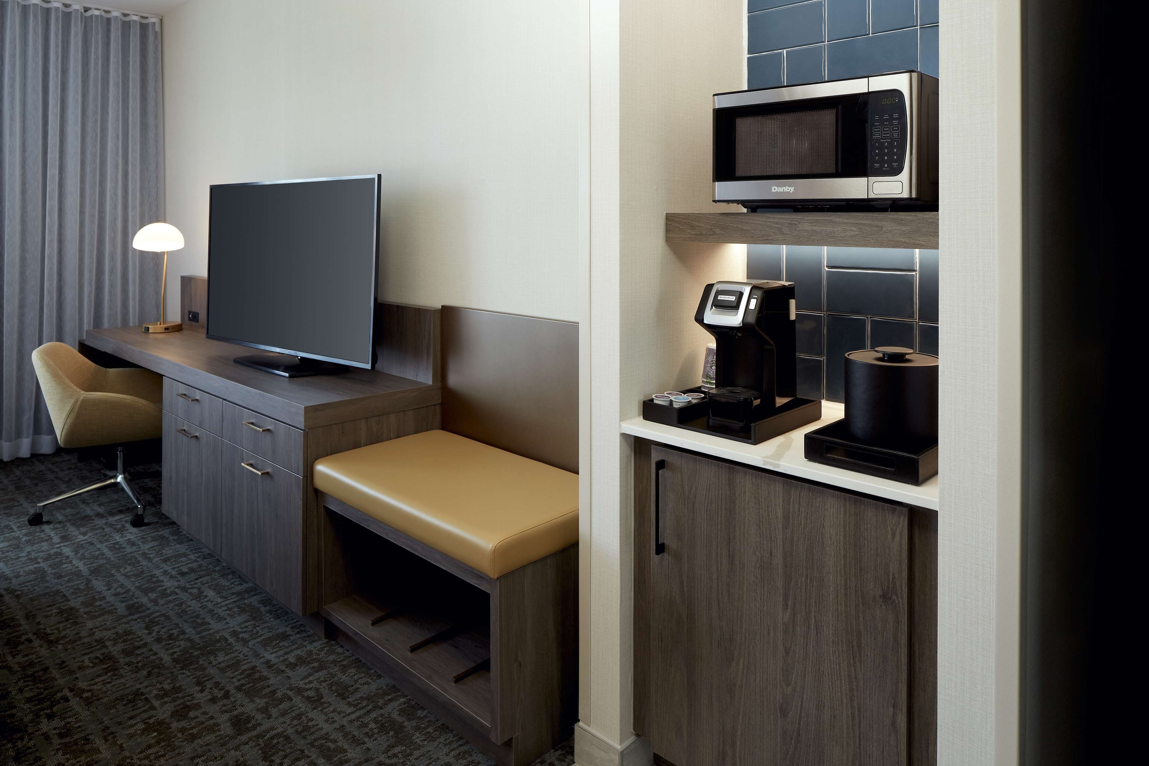 Quarto de hotel com escrivaninha, televisão, máquina de café e micro-ondas.