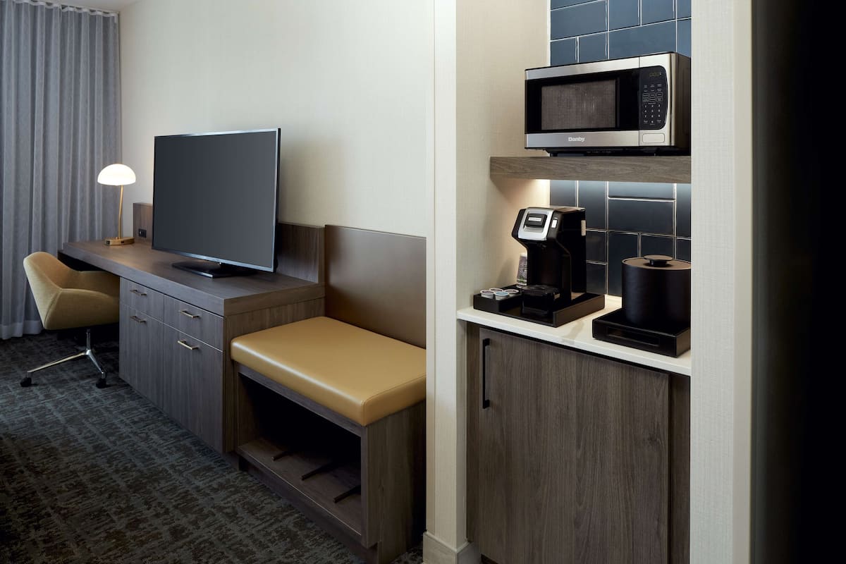 A hotel room with a desk, a television, a microwave, a coffee maker, and a seating area.