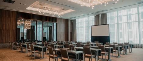 A conference room with rows of tables and chairs, a large screen, and a modern chandelier.