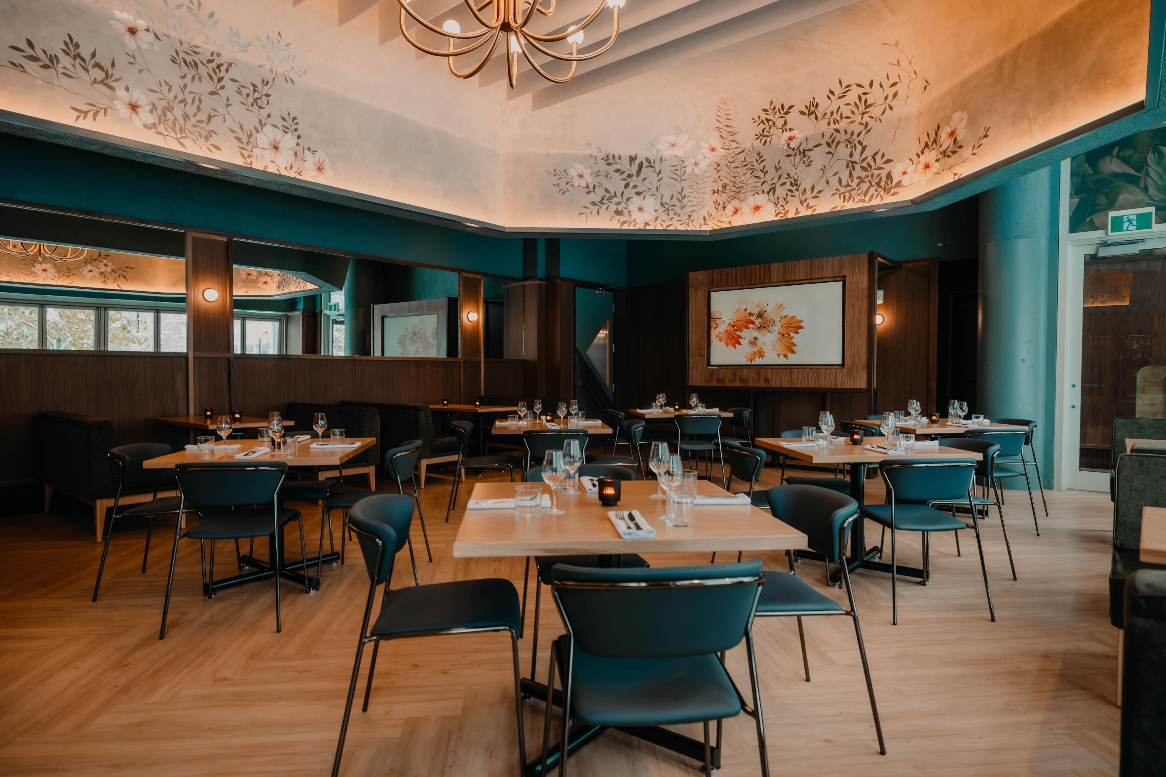A restaurant with multiple tables and chairs, a wooden floor, and a ceiling with floral patterns.