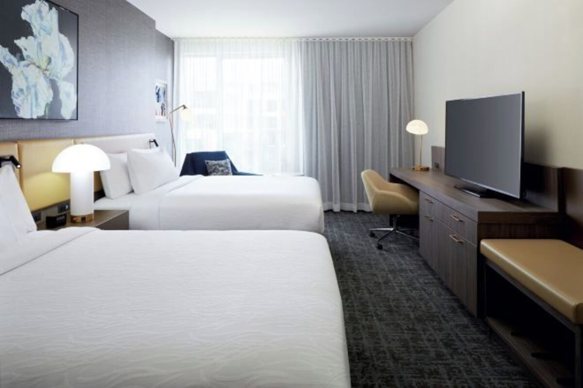 A hotel room with two beds, a TV, a desk, and a chair.