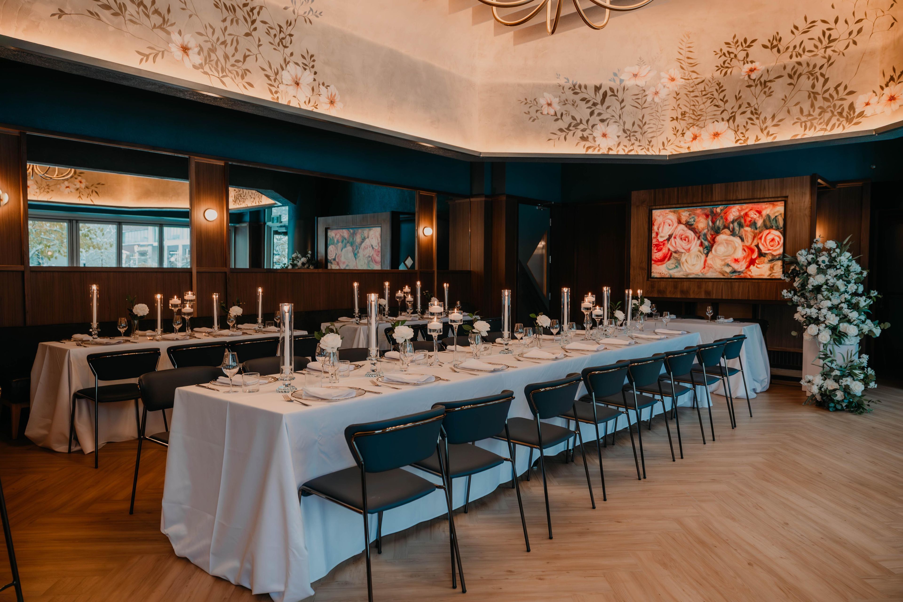 A formal dining room with long tables set for a meal, featuring white tablecloths, candles, and floral centerpieces.