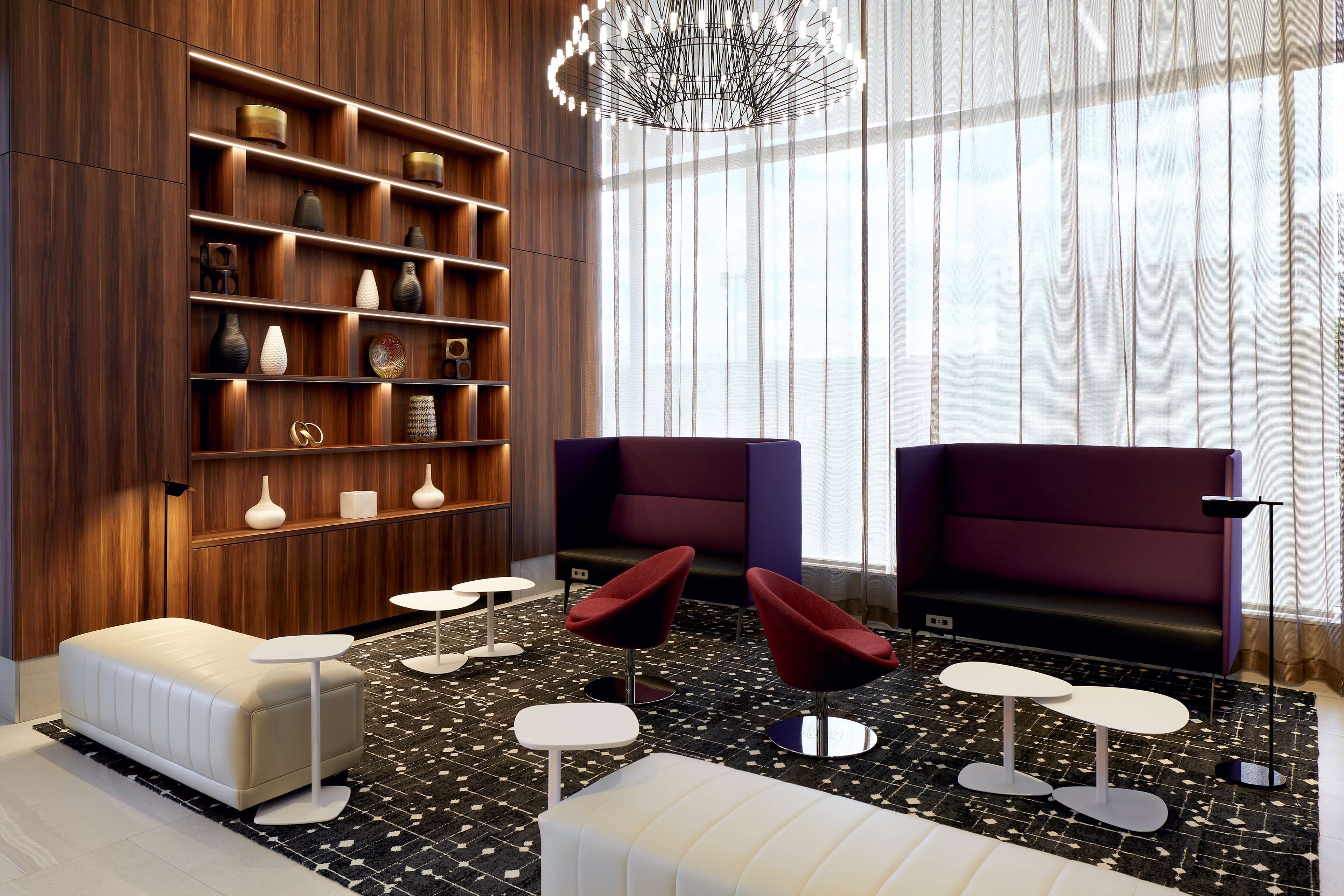 A modern lounge area with a wooden bookshelf, two purple armchairs, a white sofa, and a patterned rug.