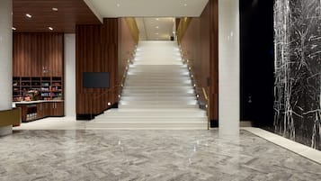 Un interior moderno con una escalera de mármol, paneles de madera y una gran pared de mármol negro.