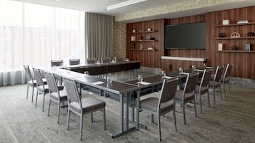 A conference room with a long table, chairs, a TV, and shelves with books and decorative items.