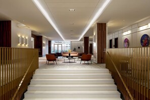 A modern hotel lobby with a staircase, seating area, and artwork on the walls. - Hilton Garden Inn Montreal Midtown (Montreal)