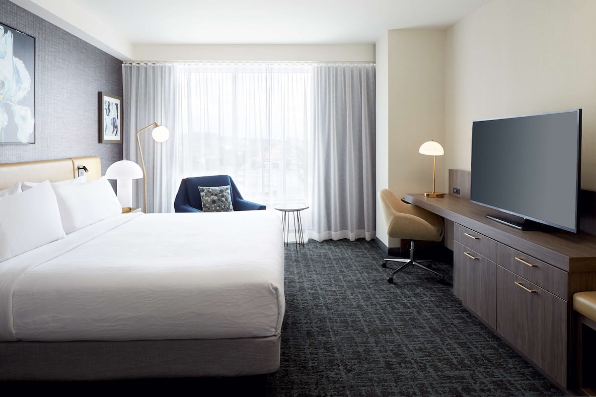 A hotel room with a large bed, a desk with a television, a chair, and a small table.
