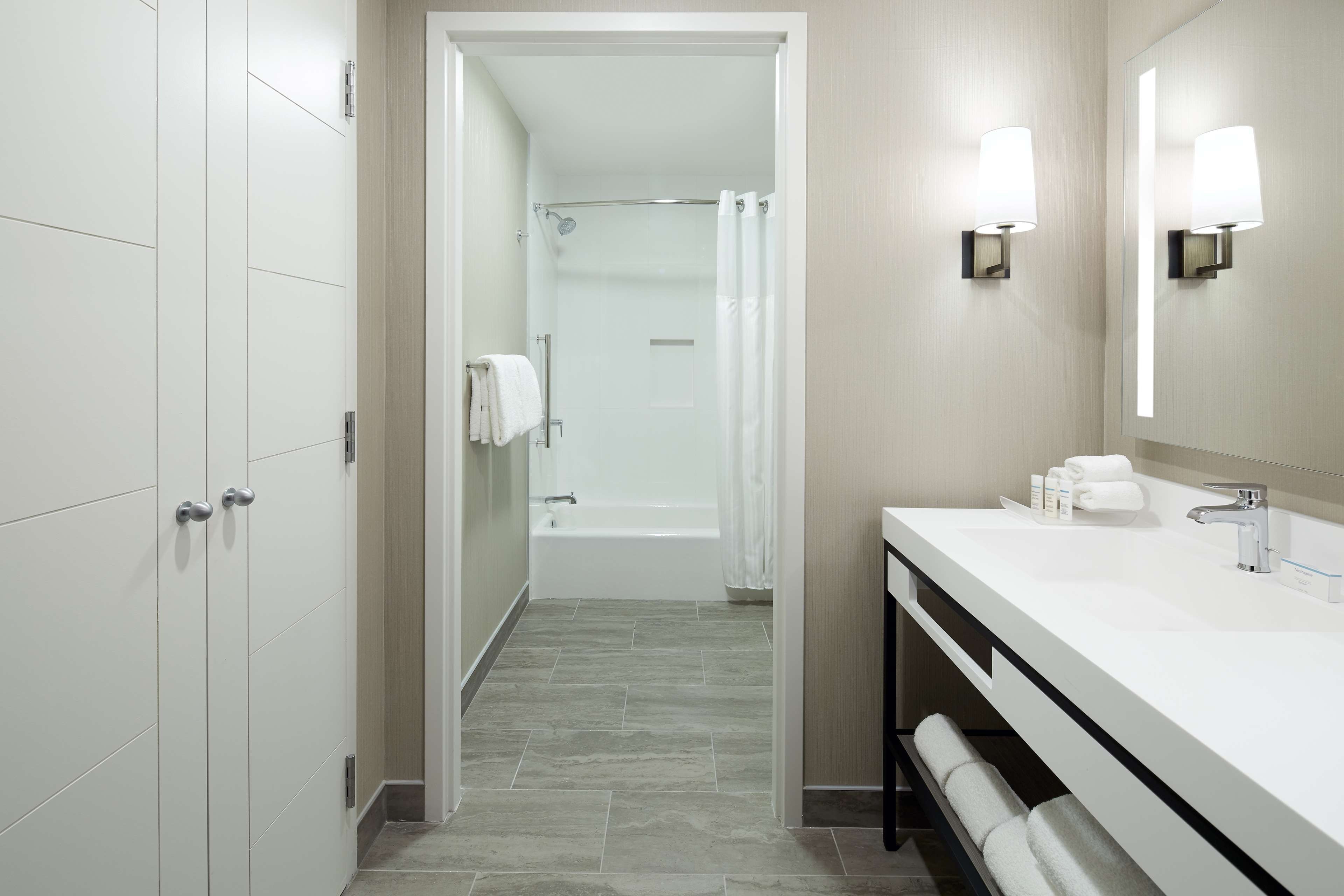 Ein modernes Badezimmer mit bodenebenen Dusche, Waschtisch mit Spiegel und Handtuchhalter.