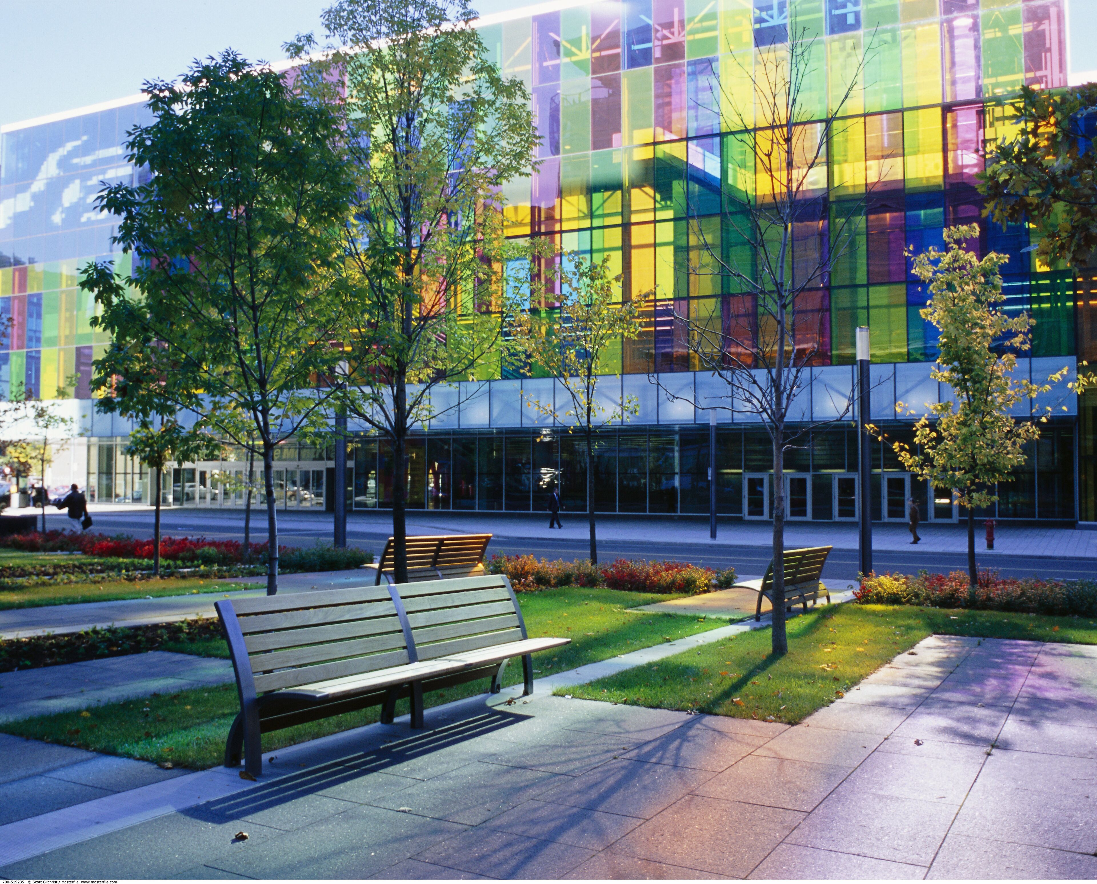 A modern building with large glass windows and benches in a landscaped area.