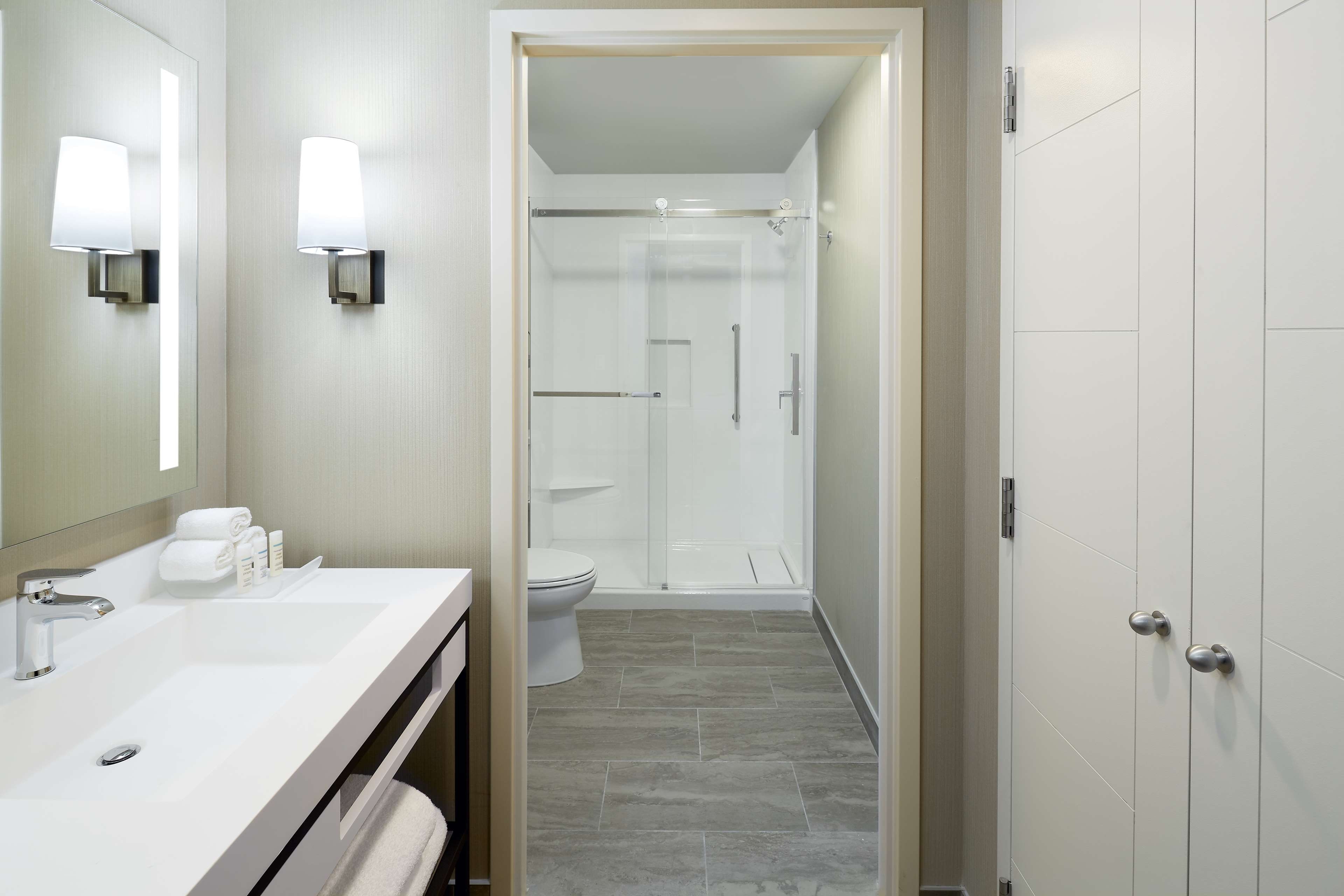 Ein Hotelbad mit einem Doppelwaschbecken, einem Spiegel, einer Dusche und einer Toilette.