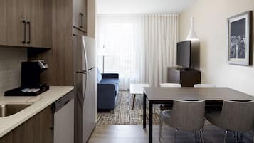 A compact hotel room with a kitchenette, a dining area, and a seating space.