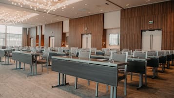 Un salón de conferencias con mesas y sillas largas, paneles de madera en las paredes y una lámpara moderna.