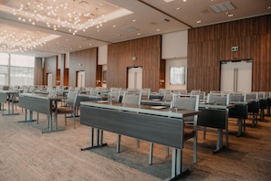 A conference room with long tables and chairs, wooden paneling on the walls, and a modern chandelier.
