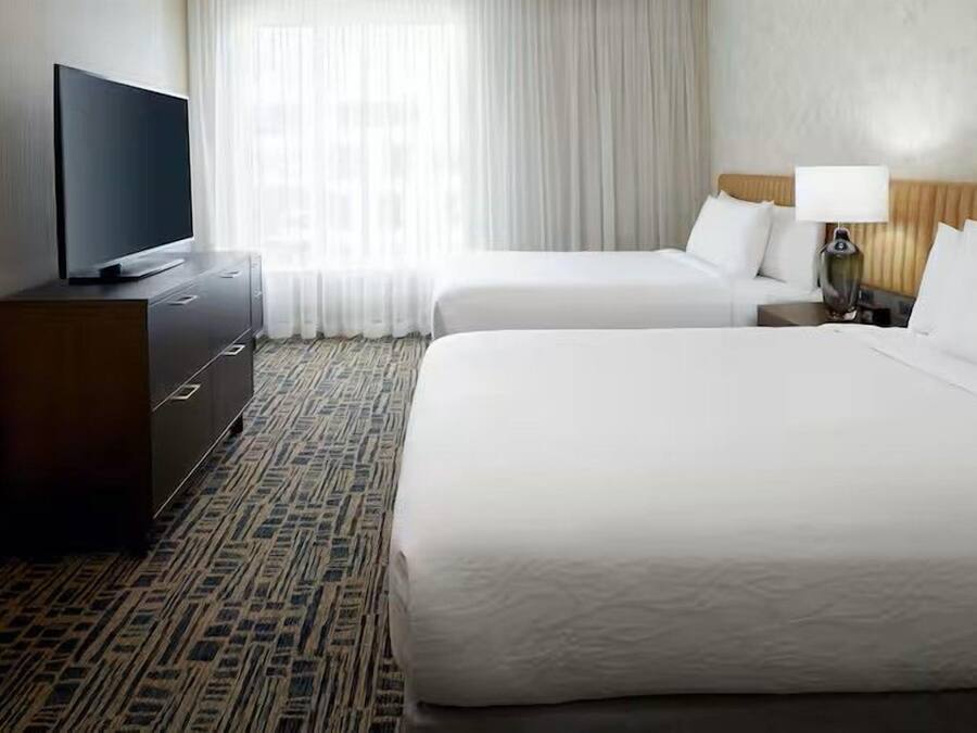 A hotel room with a large bed, a smaller bed, a TV on a dresser, and a window with curtains.