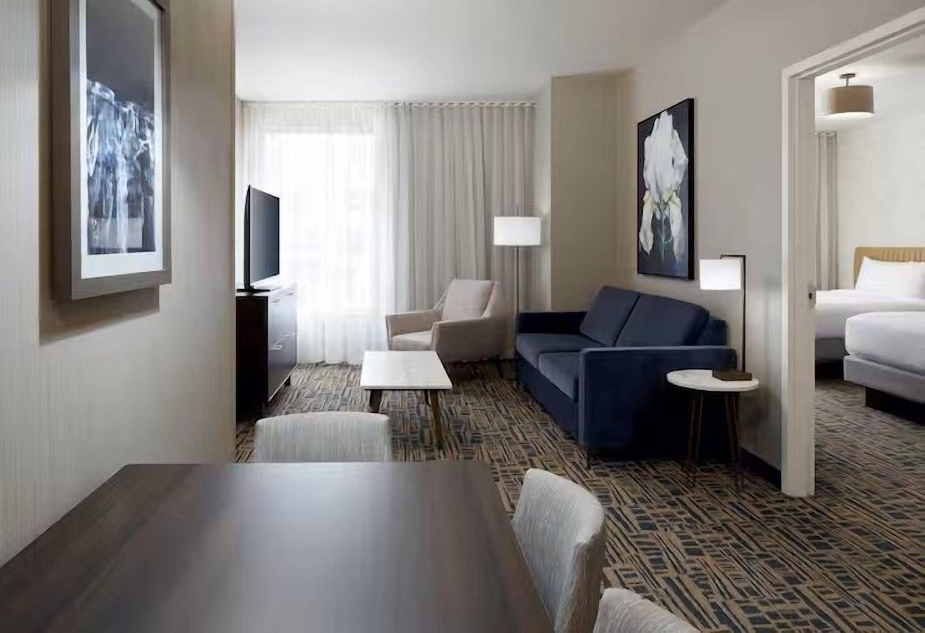 Habitación de hotel con una mesa de comedor, sofá, sillón y cama.