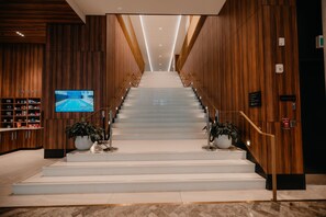 Eine Treppe in der Hotelhalle mit Holzvertäfelung an den Wänden, einem Fernseher links sowie Blumentöpfen oben und unten.