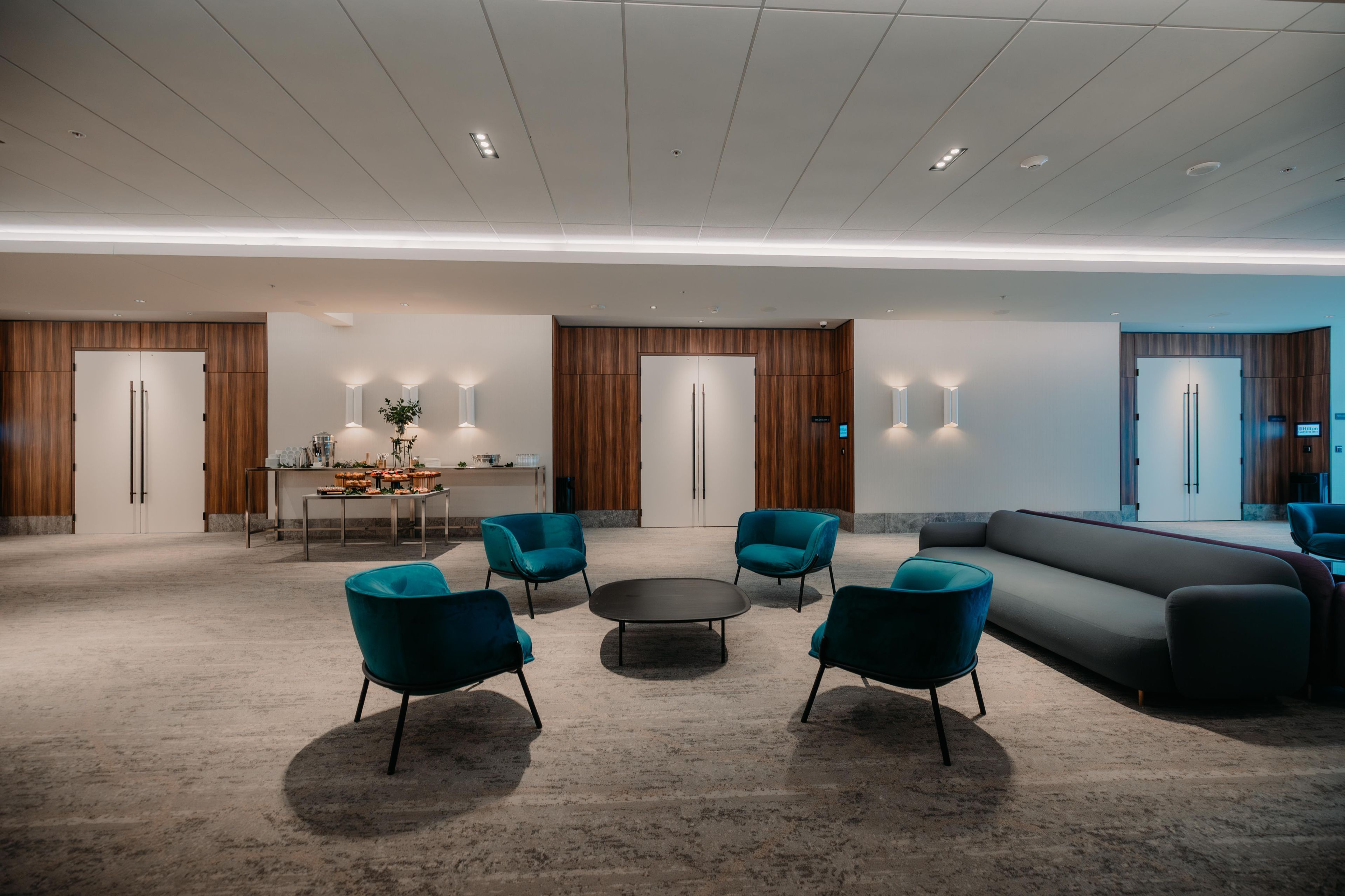 A modern lobby with a central seating area, wooden panel walls, and recessed lighting.