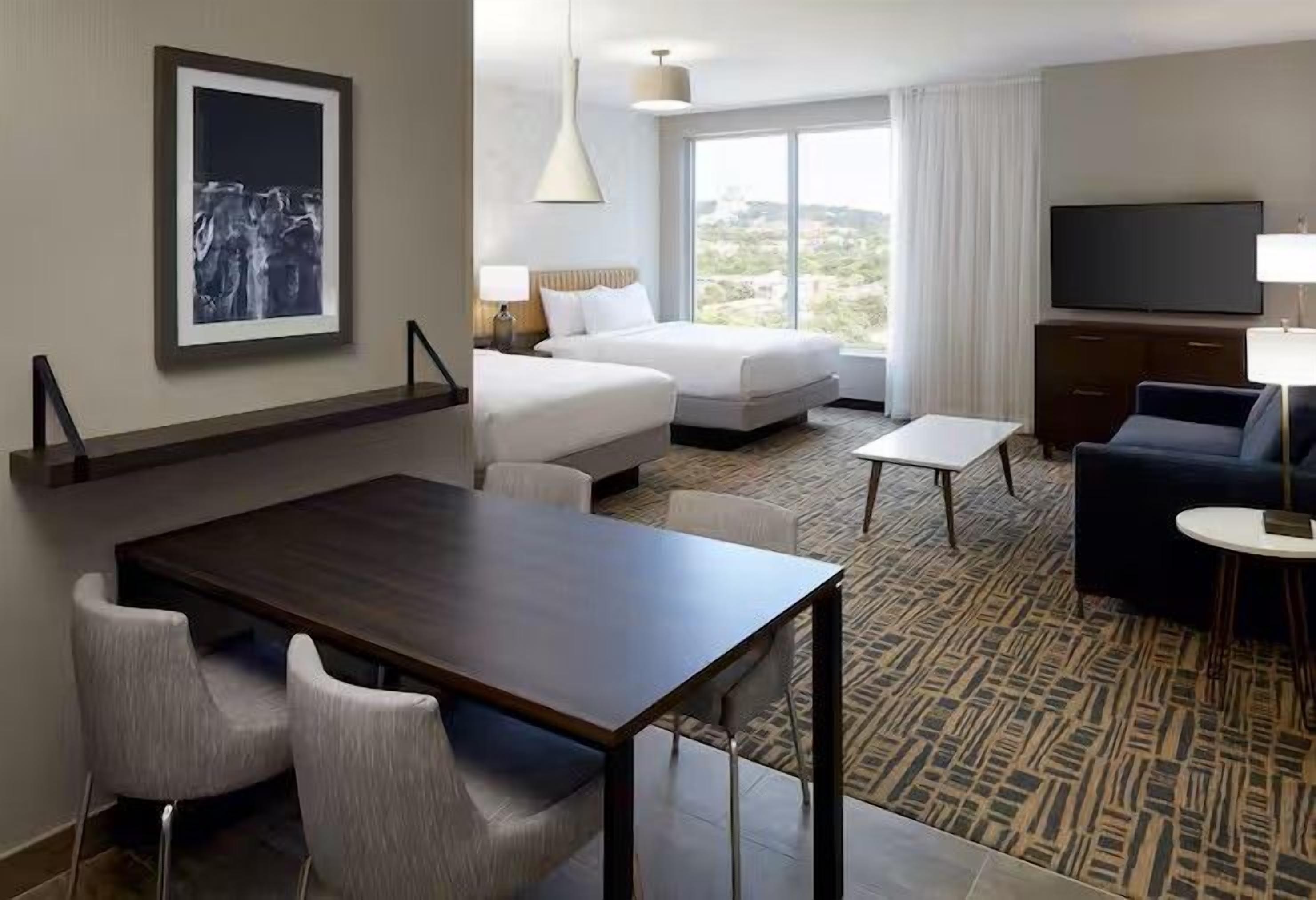 Habitación de hotel con una cama, un escritorio, una silla, un televisor y una ventana con vistas.
