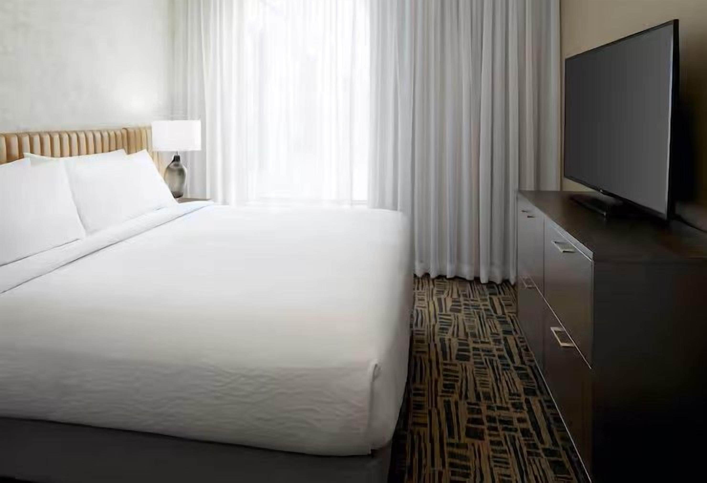 A hotel room with a large bed, a flat-screen TV, a nightstand, and a patterned carpet.