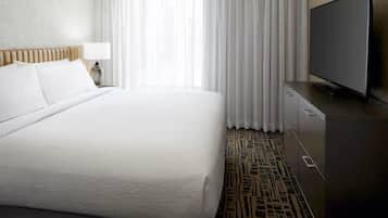 A hotel room with a large bed, a flat-screen TV, a nightstand, and a patterned carpet.