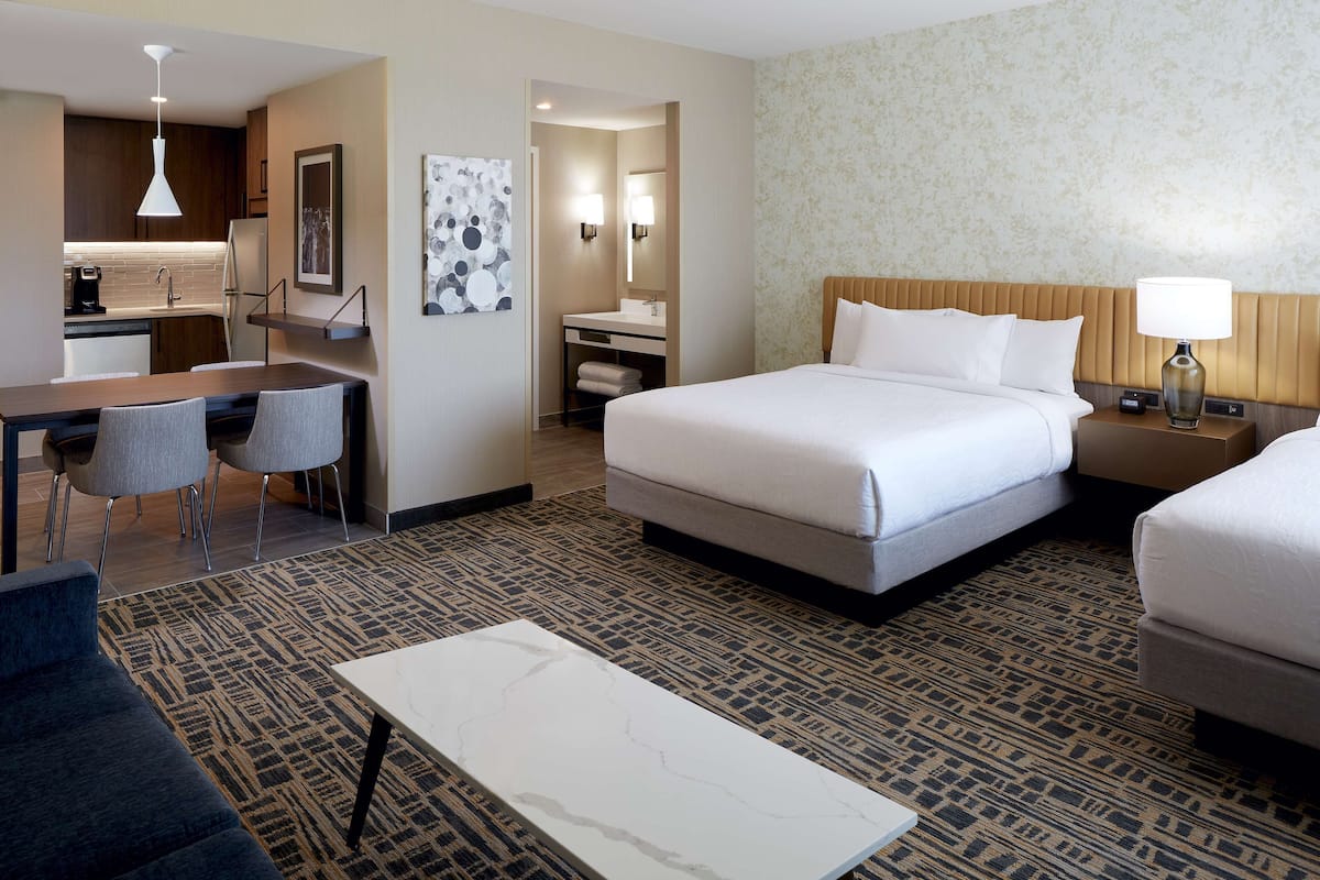 A hotel room with a bed, bedside tables, a desk with chairs, a small bathroom, and a patterned carpet.