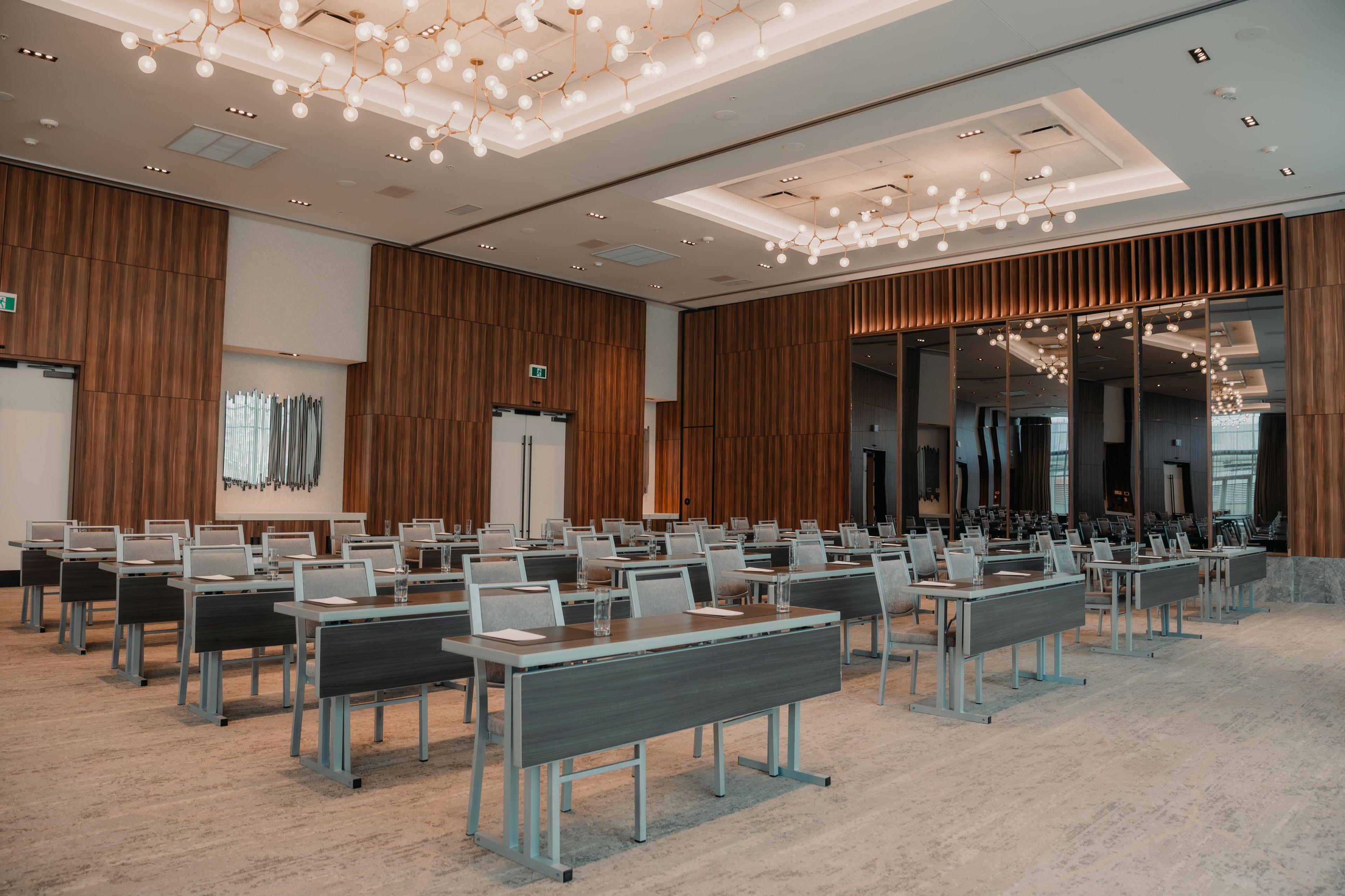 A conference room with rows of tables and chairs, wooden paneling on the walls, and a modern chandelier.