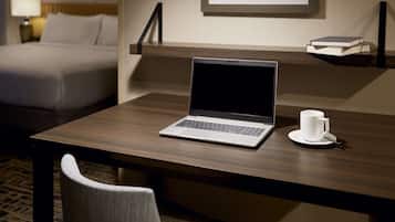 Une chambre d’hôtel avec un lit, un bureau avec un ordinateur portable, une tasse et un tableau encadré au mur.