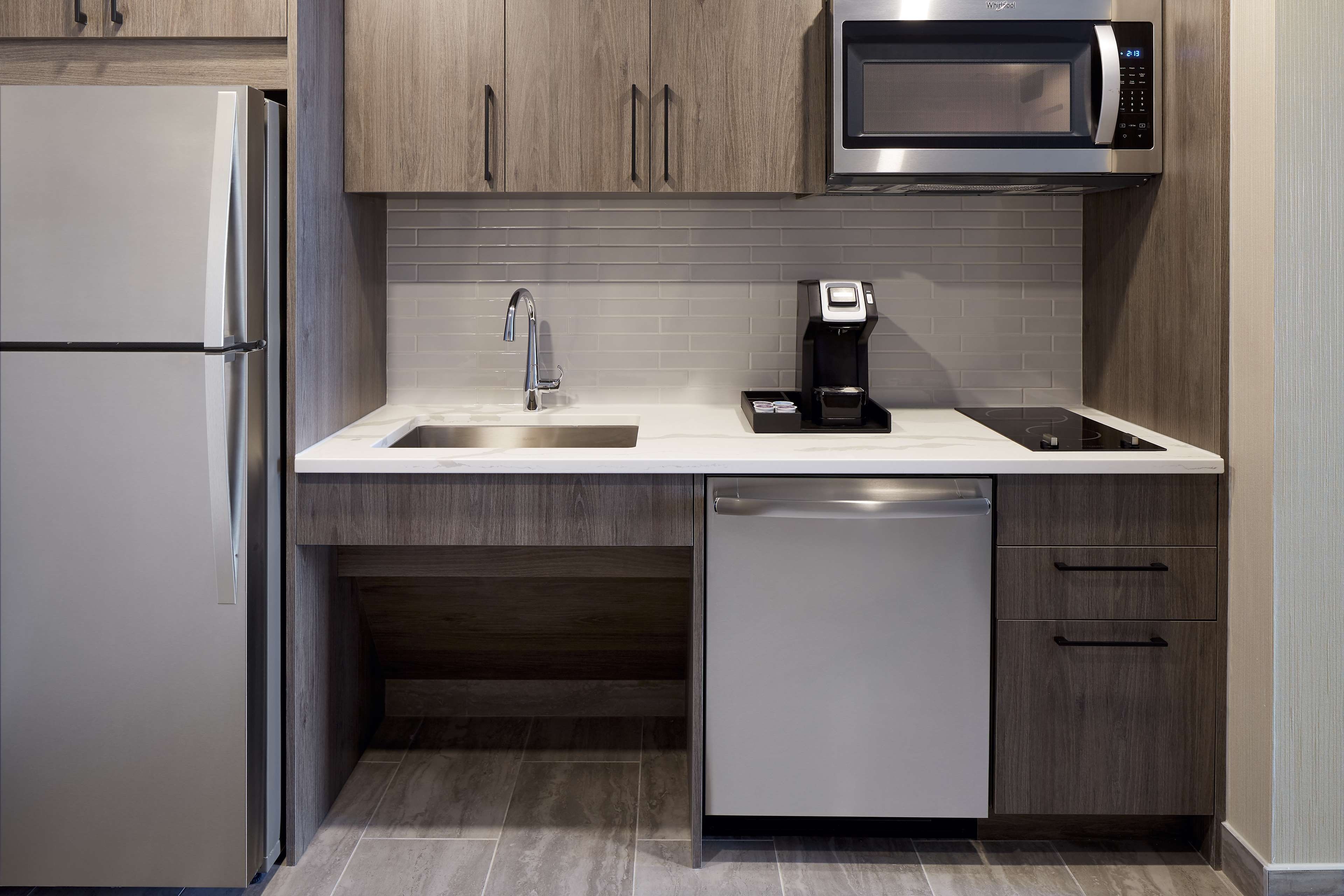 Una cocina moderna con un refrigerador de acero inoxidable, un microondas, una cafetera, un lavamanos y un lavavajillas.