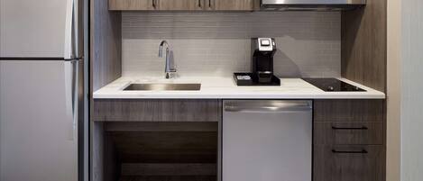 Una cocina moderna con un refrigerador de acero inoxidable, un microondas, una cafetera, un lavamanos y un lavavajillas.