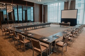 Ein Konferenzraum mit einem langen Tisch, Stühlen, einer Projektionsleinwand und großen Fenstern.