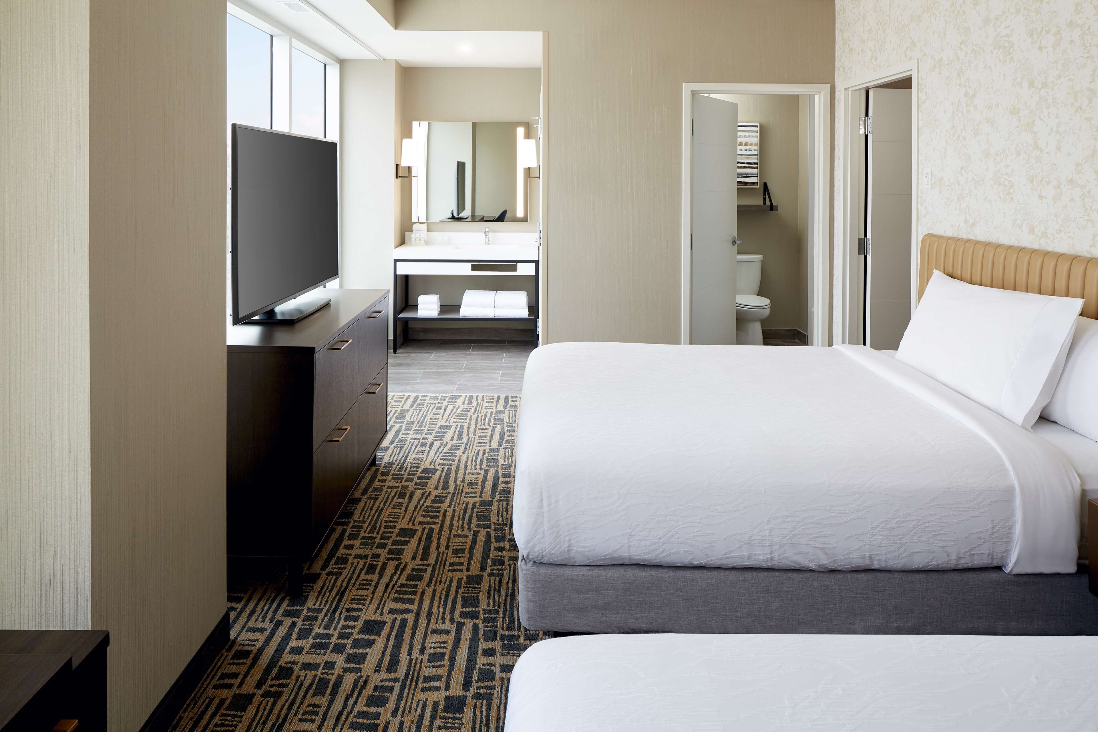 Una habitación de hotel con cama, televisión, baño y un pasillo.