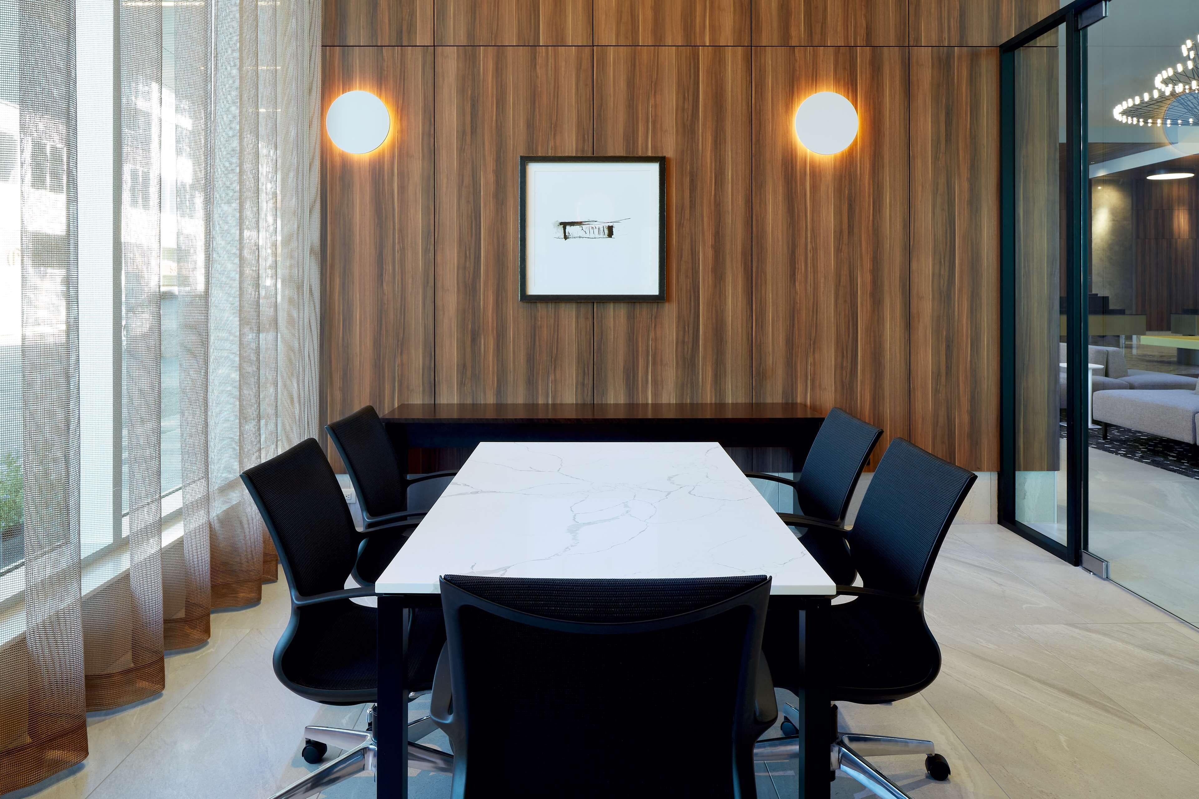 Un salón de conferencias con una mesa blanca, sillas negras y un cuadro en la pared.