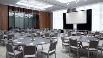 Un salón de conferencias con mesas redondas, sillas, una pantalla grande y una lámpara de araña moderna.