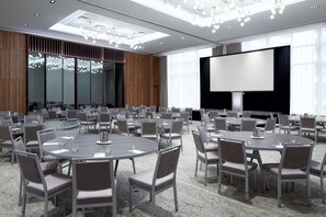 Un salón de conferencias con mesas redondas, sillas, una pantalla grande y una lámpara de araña moderna.