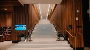 Una escalera en el vestíbulo de un hotel, con paneles de madera en las paredes, un televisor a la izquierda y plantas en macetas en la parte superior e inferior.