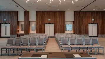 A conference room with rows of chairs, a long table, and a ceiling with hanging lights.