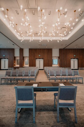 Une salle de conférence avec des rangées de chaises, une longue table et un plafond orné de luminaires suspendus.
