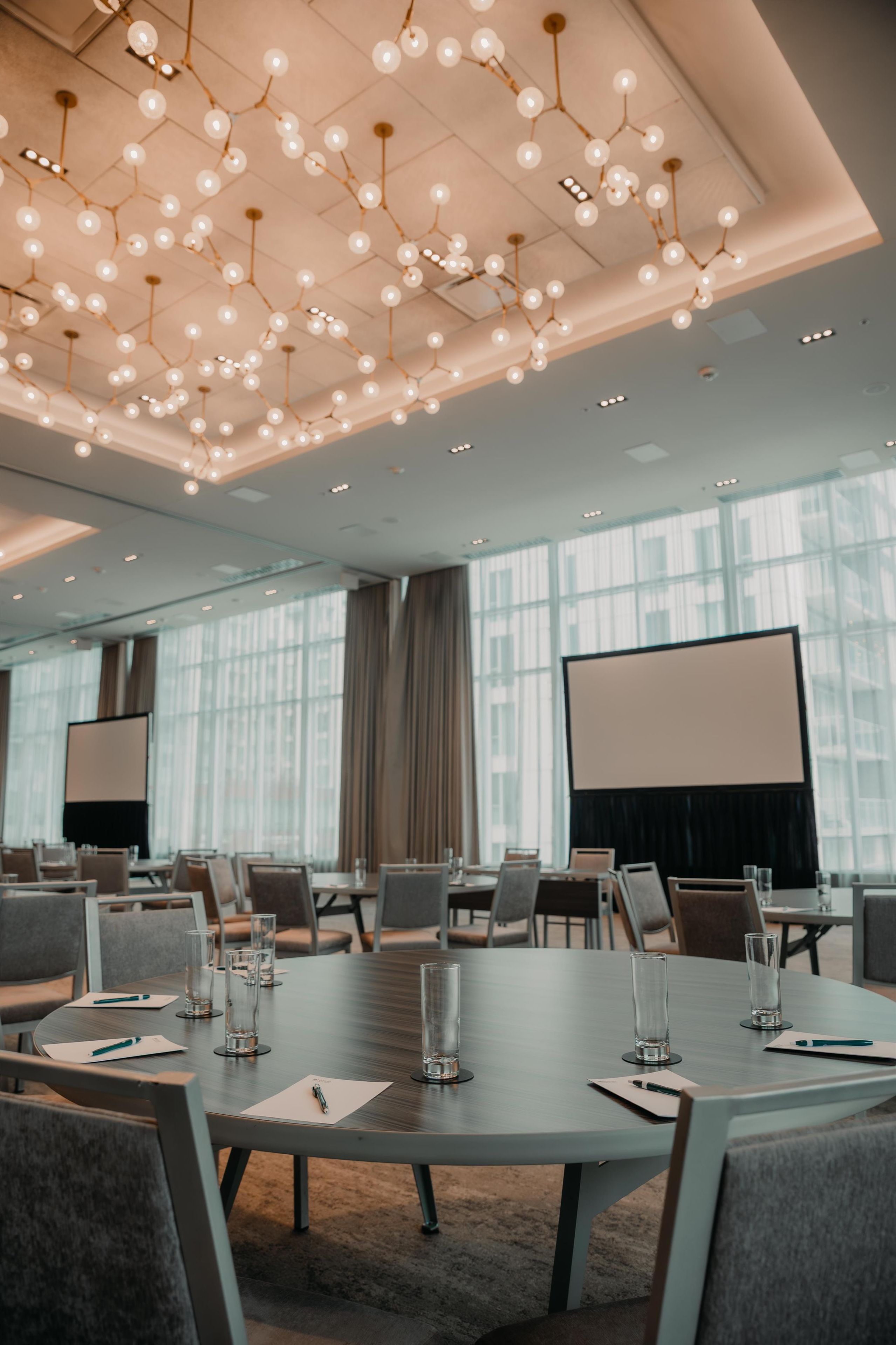 A conference room with a large table, chairs, a projector screen, and a modern ceiling light fixture.