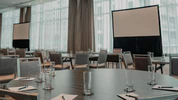 A conference room with a large table, chairs, a projector screen, and a modern ceiling light fixture.