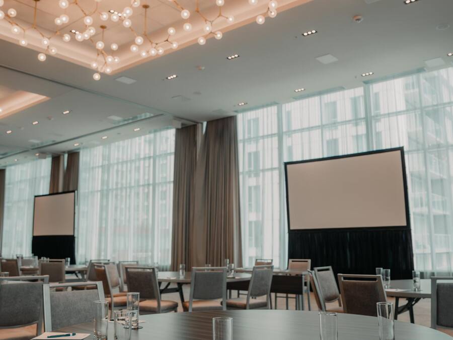 A conference room with a large table, chairs, a projector screen, and a modern ceiling light fixture.