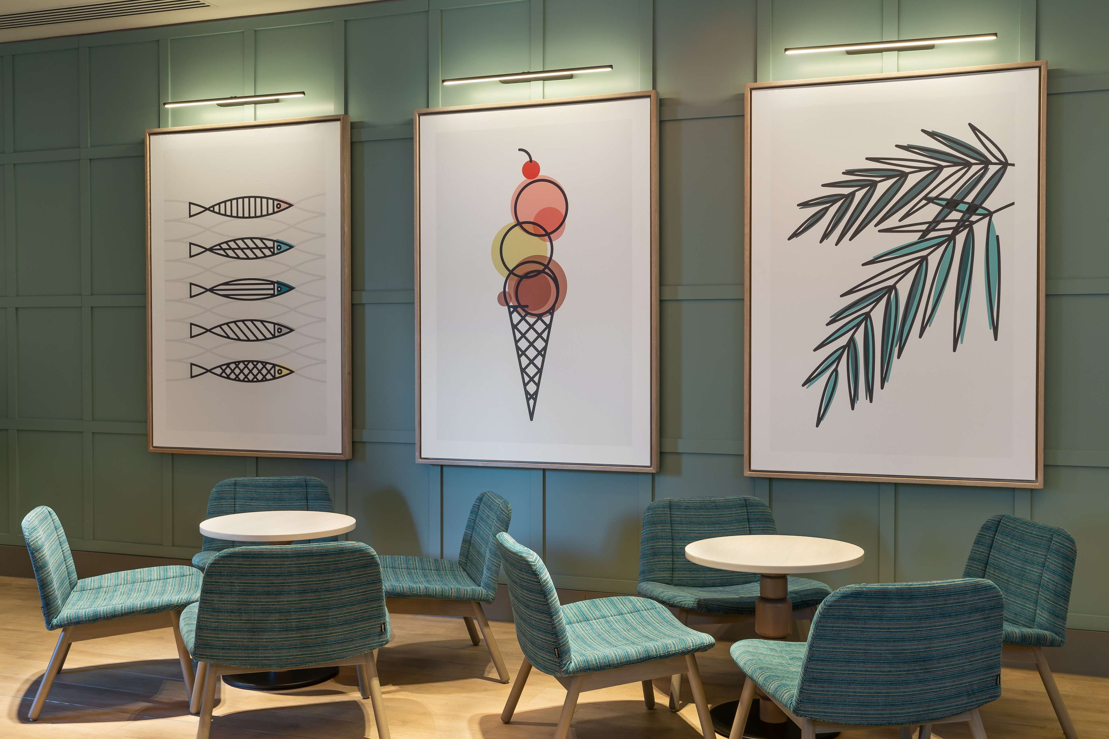 A modern interior with teal chairs and tables, framed artwork on the walls, and a wooden floor.