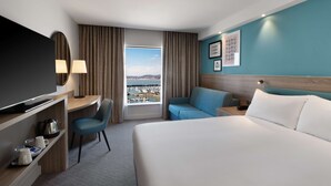 A hotel room with a bed, a desk, a chair, a TV, and a view of the harbor. - Hampton by Hilton Torquay (Torquay)
